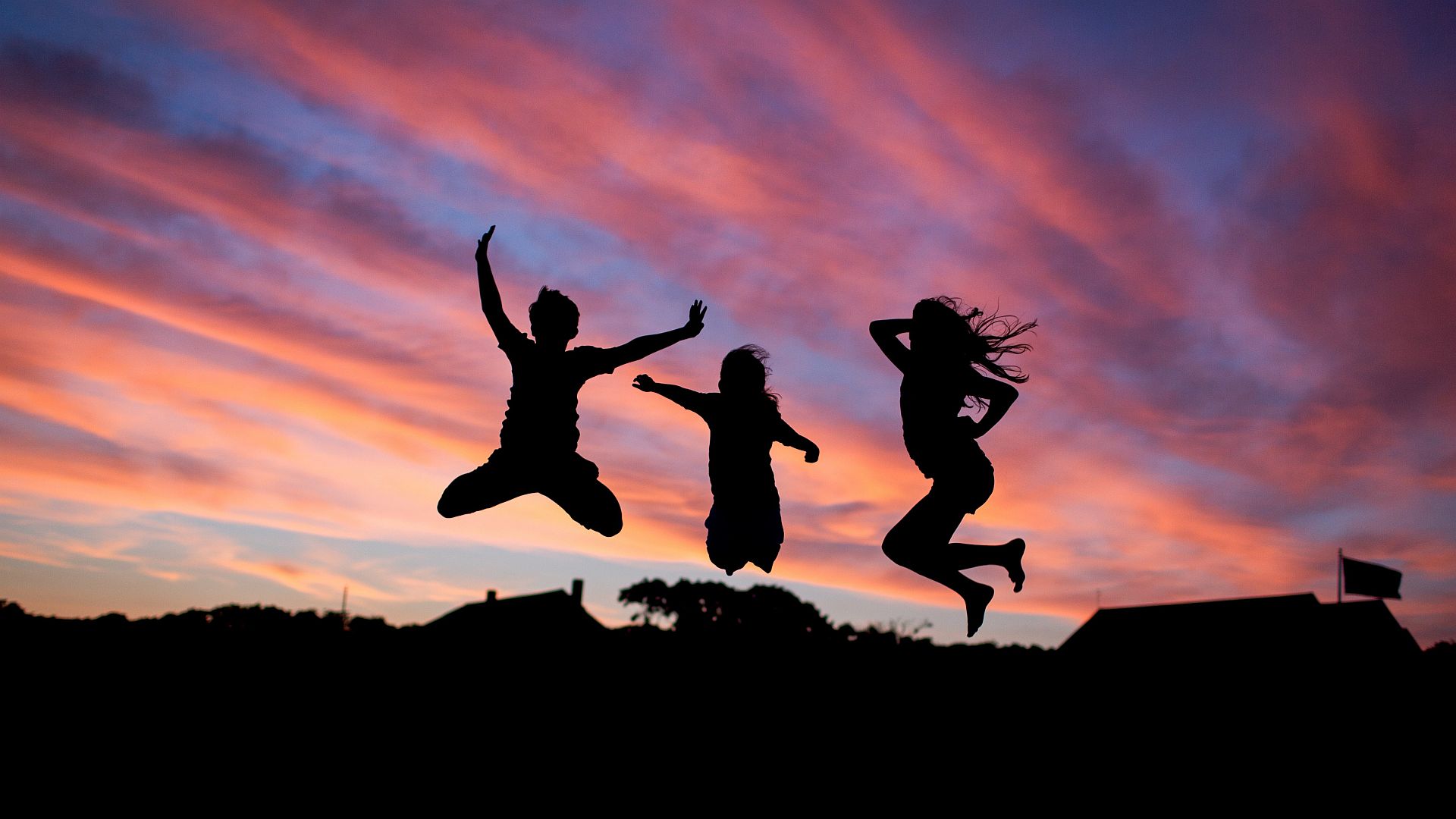 Silhouette of three children jumping on a trampoline at dusk.