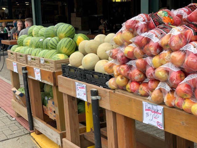 A line of tables with melons and apples on them at a farmer's market .