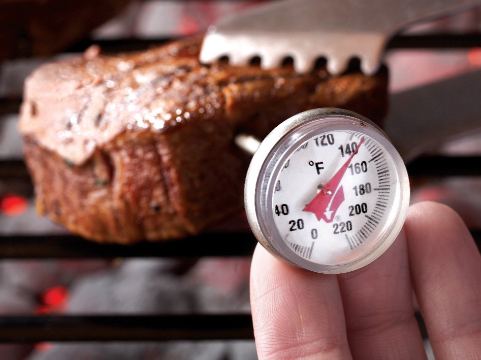 Image of a steak on a grill with a hand holding a thermometer taking the steaks temperature...