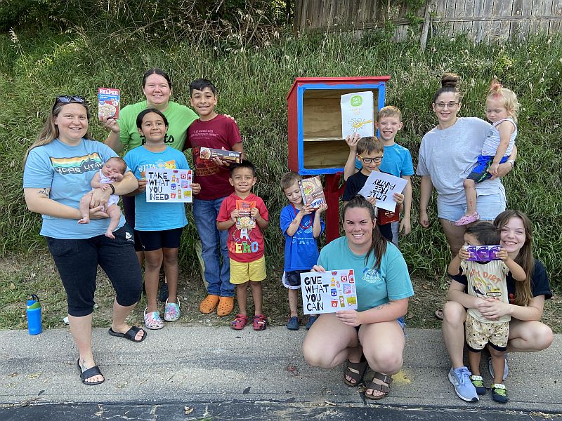 Adults and children in front of a little free pantry.