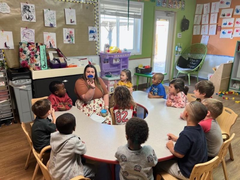 A woman teaching nutrition to a group of children sitting at a round table in a classroom.