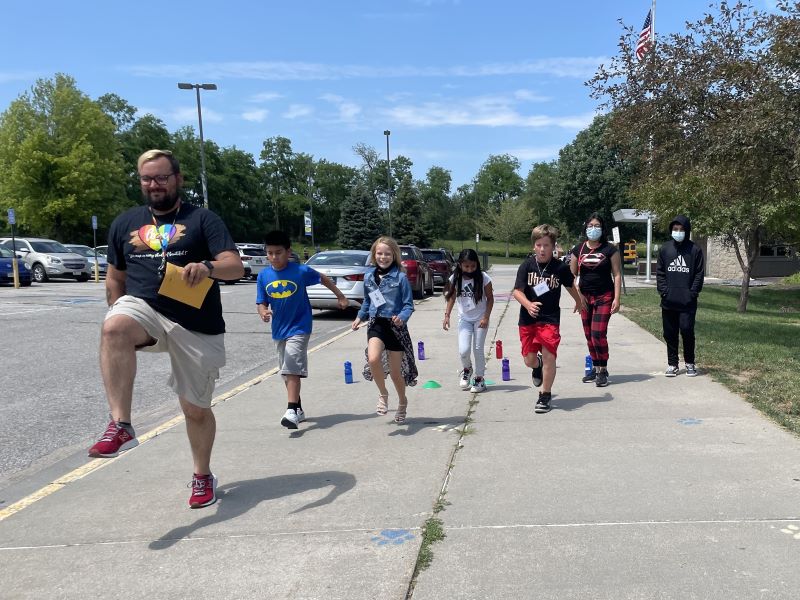 Male teacher walking with 5th grade students outside a school.