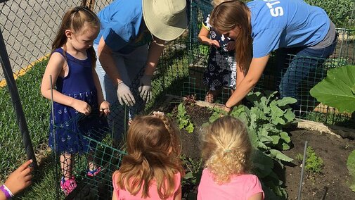 Adults and children working in a raised vegetable garden.