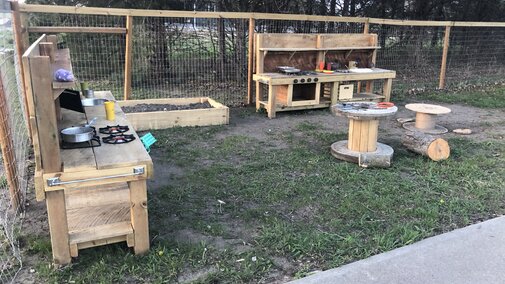 Outdoor play area for children with two play kitchens and tables.