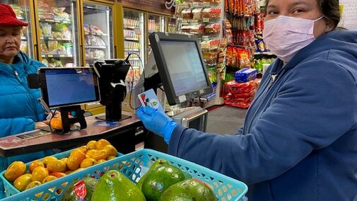 A female cashier excepting payment from a woman for groceries at a grocery store.