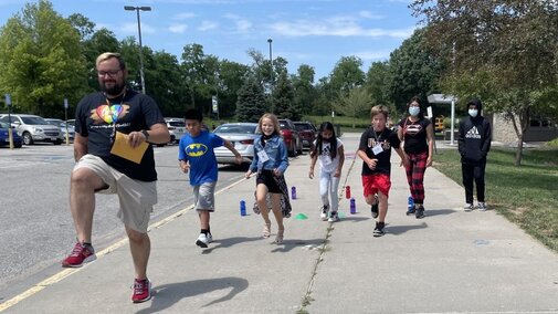 Male teacher walking with 5th grade students outside a school.